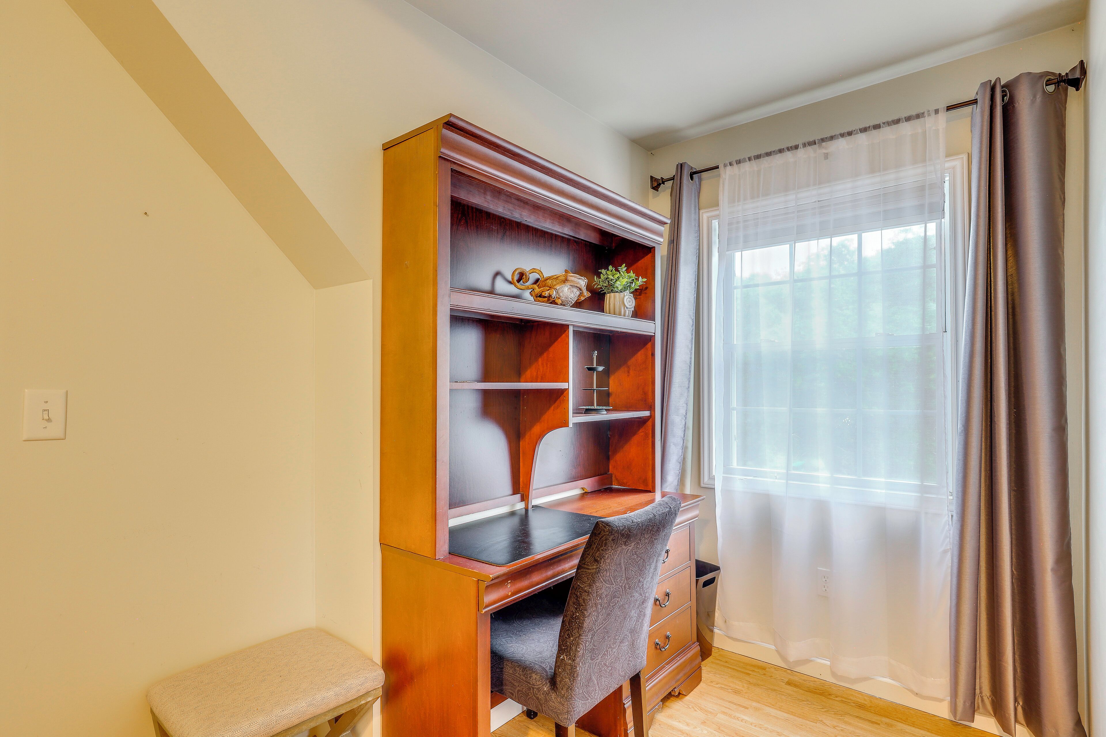 Une pièce comprenant un bureau en bois, une chaise, une étagère ornée d’objets décoratifs et une fenêtre avec des rideaux.