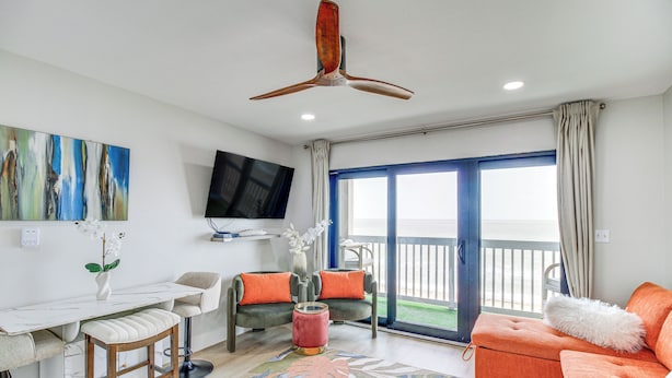 Sala de estar com televisão, ventilador de teto, sofá, mesa de centro e vista através de uma porta de vidro.