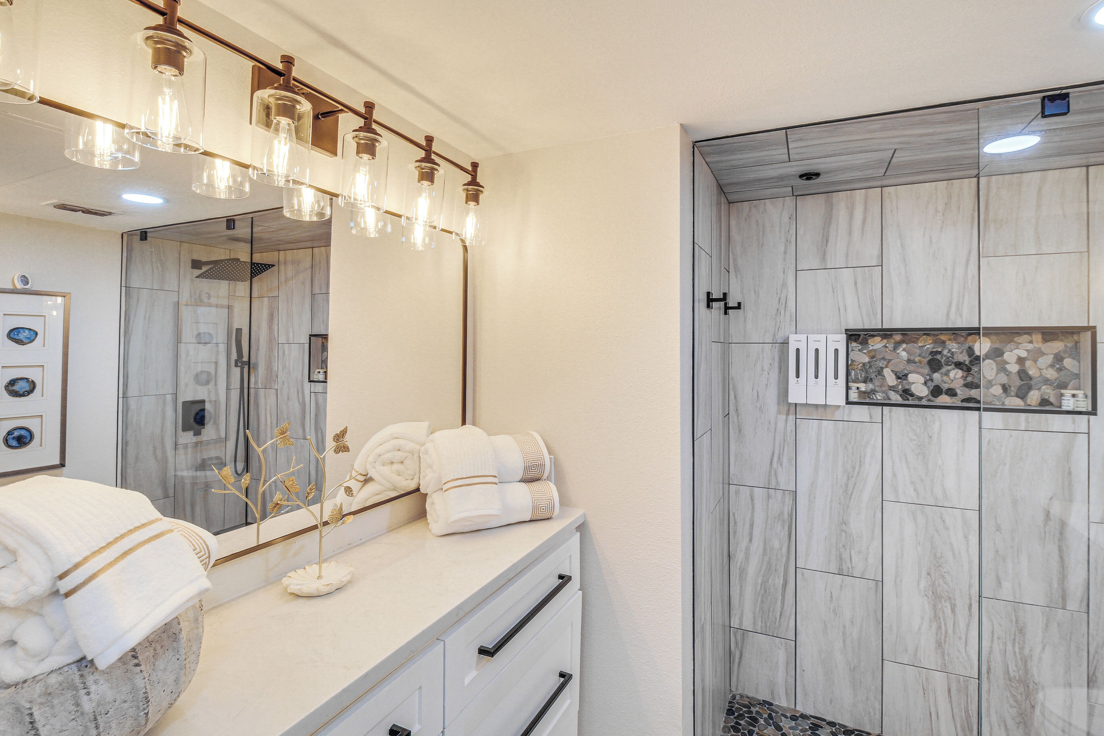 Een moderne badkamer met een grote spiegel, een wastafelmeubel met een marmeren aanrechtblad en een douche met een stenen wand.