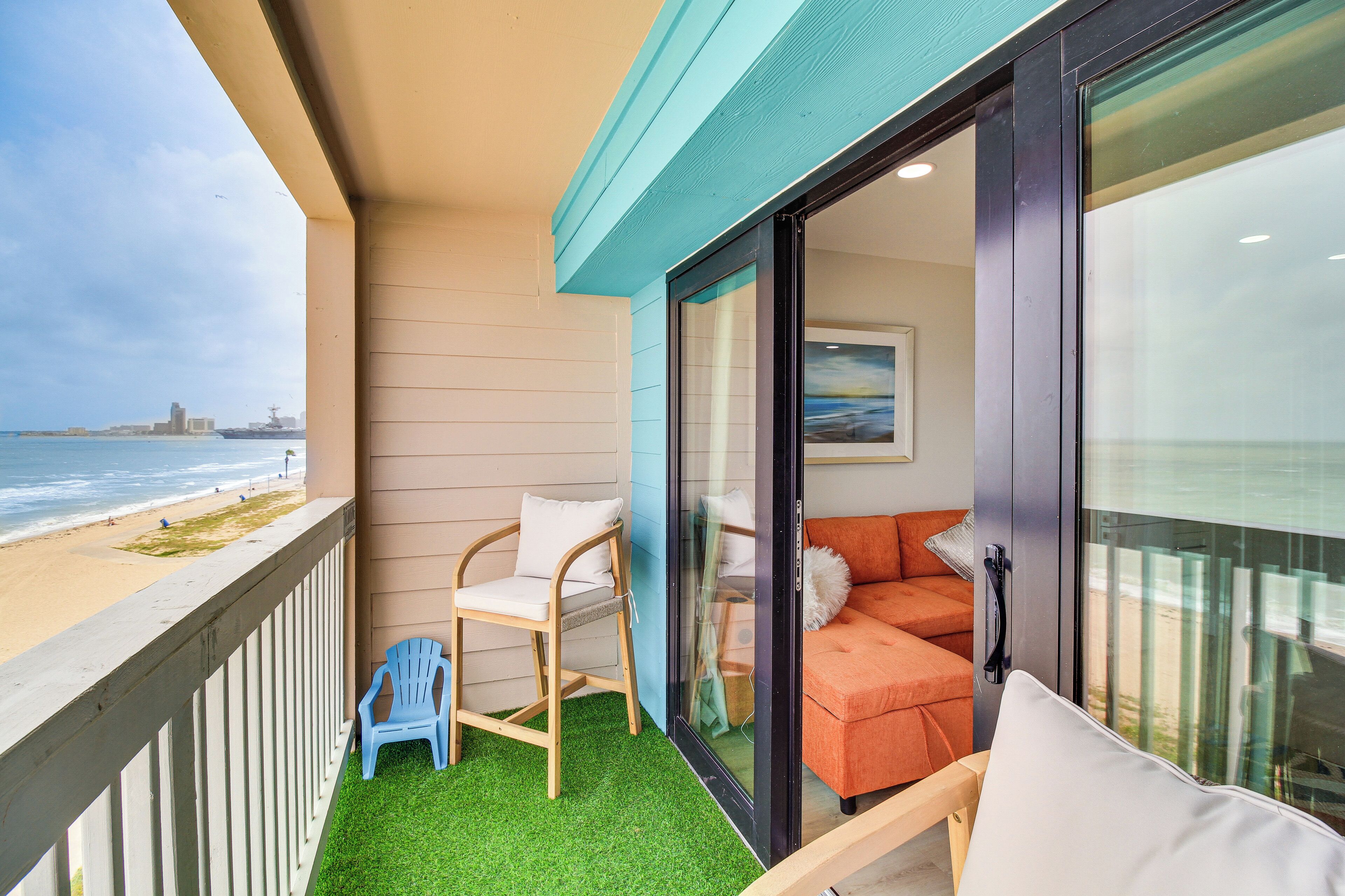 A balcony with a view of the beach, a chair, a sofa, and a glass door.
