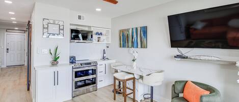 Une cuisine moderne avec des meubles blancs, un four encastré et un coin repas comprenant une table et des chaises blanches.