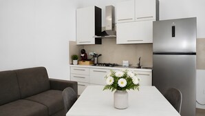 A modern kitchen with white cabinets, a stainless steel refrigerator, a dining table with a vase of flowers, and a gray sofa. - Holiday Home 'Vacanza Via Roma 103 F' with Sea View and Wi-Fi (Crotone)