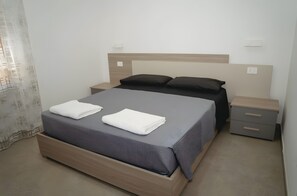 Un lit bien fait, avec une tête de lit, deux tables de chevet et un rideau à moitié tiré.