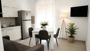A modern kitchen with white cabinets, a built-in refrigerator, a dining table with chairs, a potted plant, and a floor lamp. - Holiday Home 'Vacanza Via Roma 103 F' with Sea View and Wi-Fi (Crotone)