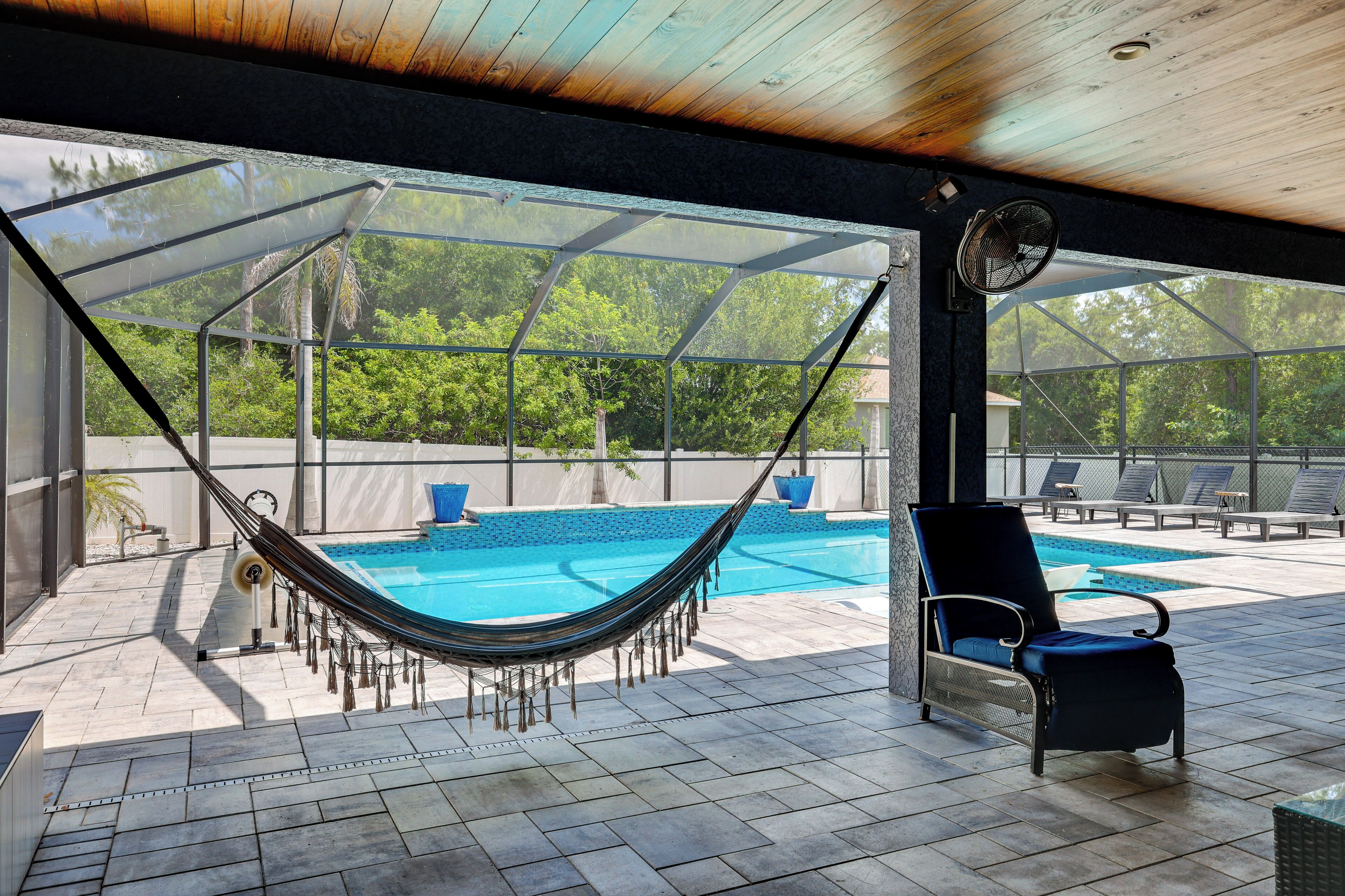 A covered outdoor area with a pool, a hammock, and lounge chairs.