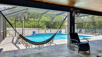 A covered outdoor area with a pool, a hammock, and lounge chairs.