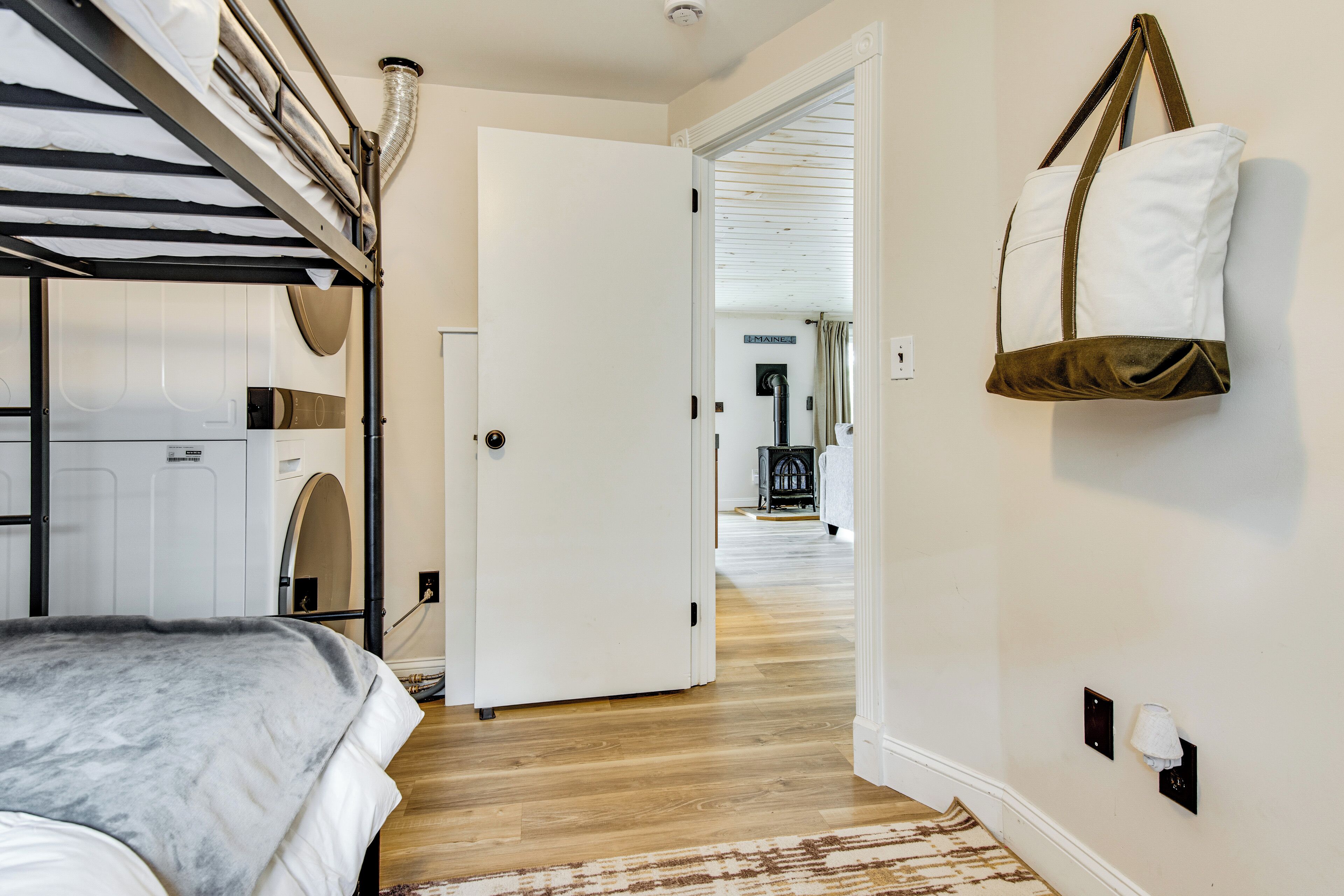 A bedroom with a bunk bed, a white door, a hallway leading to a dining area, and a wall-mounted bag.