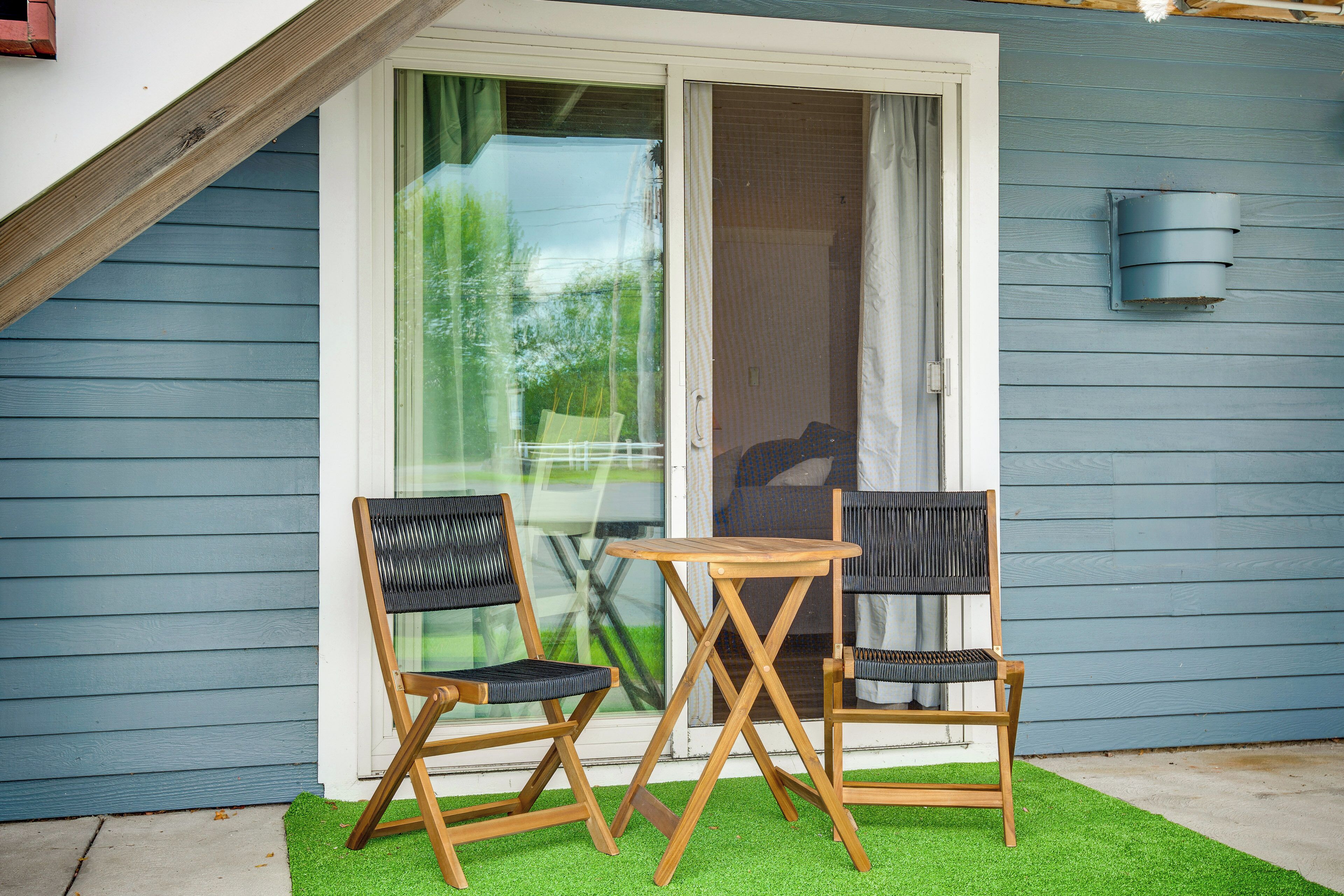 A patio with two wooden chairs and a small table, a sliding glass door, and a blue exterior wall.