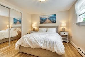 A bedroom with a bed, bedside tables, a painting, and a window. - Walk to Wells Beach! Family-friendly Gem w/ Patio (Wells)