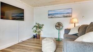 Un salon avec un téléviseur à écran plat, un tableau, un ventilateur, un canapé et une plante en pot.