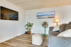A living room with a flat-screen TV, a painting, a fan, a sofa, and a potted plant. - Walk to Wells Beach! Family-friendly Gem w/ Patio (Wells)