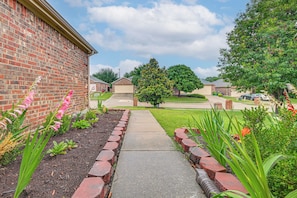 A residential driveway with a brick pathway leading to a house, surrounded by well-maintained gardens and trees. - Great for Traveling Nurses! Charming Mckinney Home (McKinney)