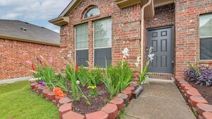 A brick building with a grey door, large windows, and a flower bed in front. - Great for Traveling Nurses! Charming Mckinney Home (McKinney)