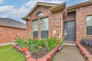 A brick building with a grey door, large windows, and a flower bed in front. - Great for Traveling Nurses! Charming Mckinney Home (McKinney)