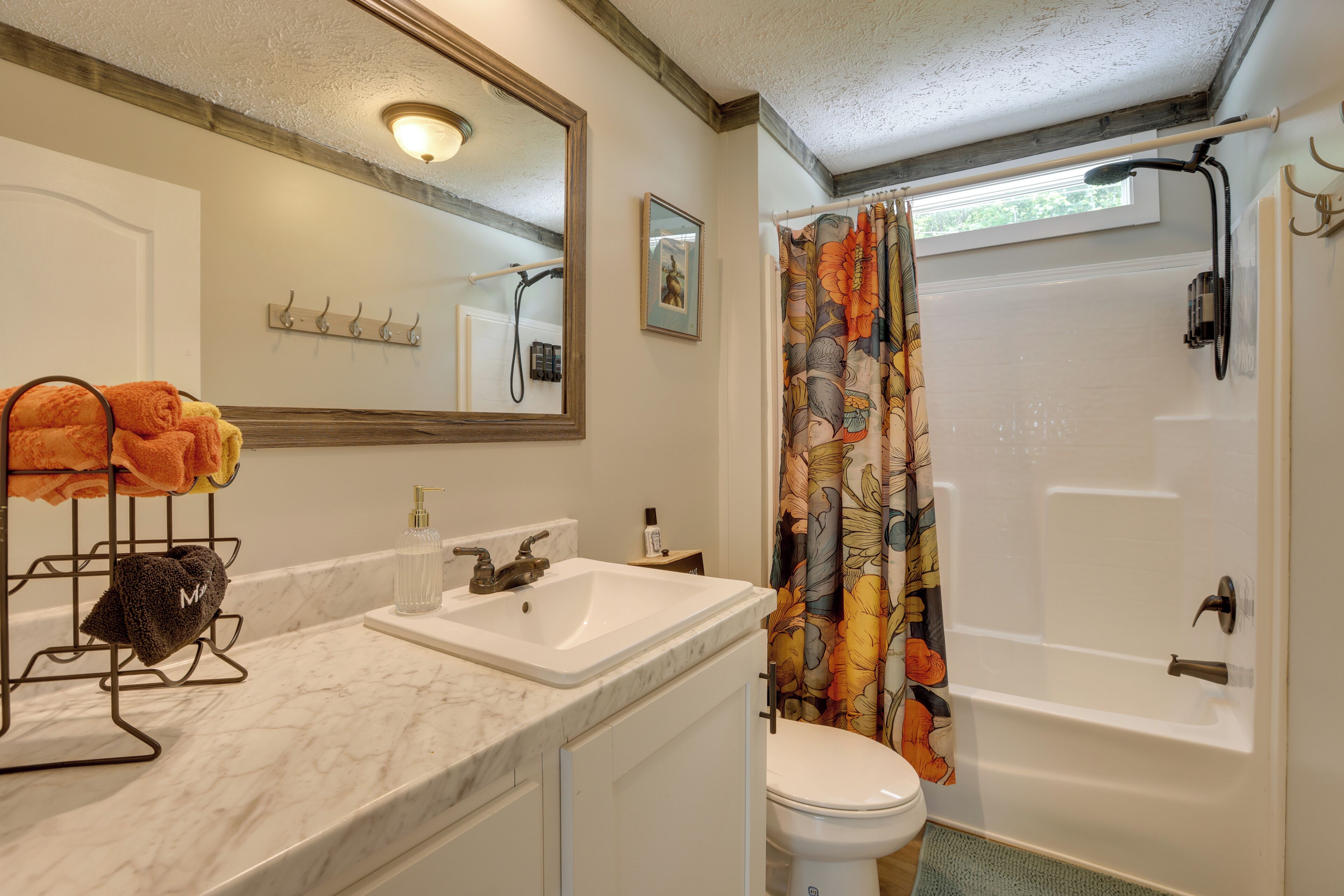 Un baño con un lavabo blanco, un inodoro, una ducha con cortina estampada con motivos florales y un espejo sobre el lavabo.