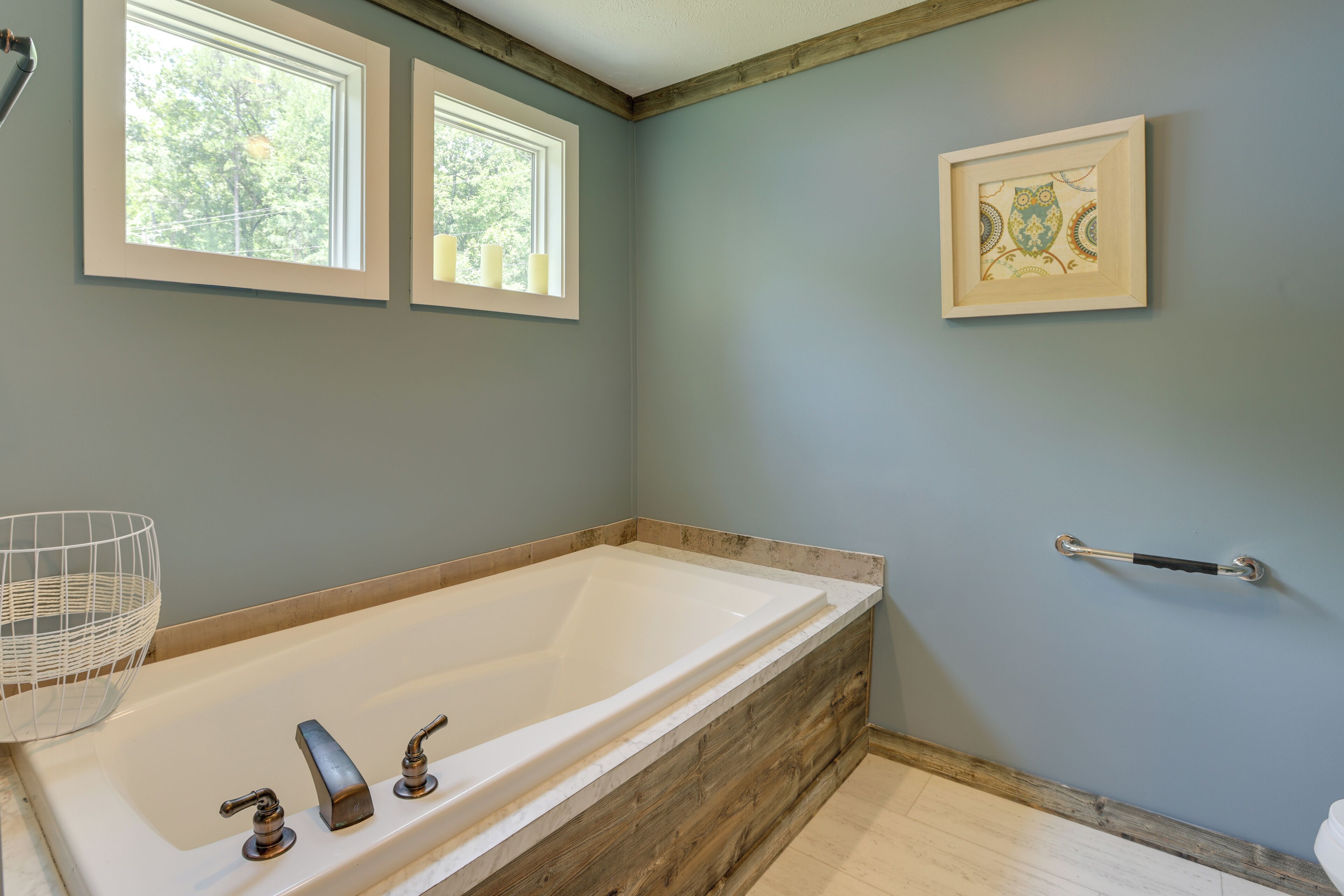 Un baño con bañera de madera, dos ventanas, una obra de arte enmarcada y un pasamanos.