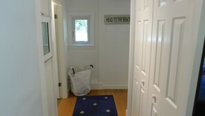 Un couloir avec une porte sur la droite, une fenêtre au-dessus de laquelle est apposée une enseigne, et une poubelle dans le coin.