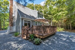 A two-story house with a wooden deck, a brick chimney, and a gravel driveway. - Barnstable Vacation Base Near Beaches & Hyannis RPAM125 (Centerville)
