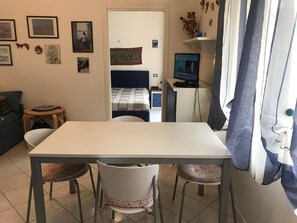 A small, well-lit room with a white table, two chairs, a bed with a patterned blanket, and a desk with a computer. - La Terrasse - Matteotti 110 (Ospedaletti)