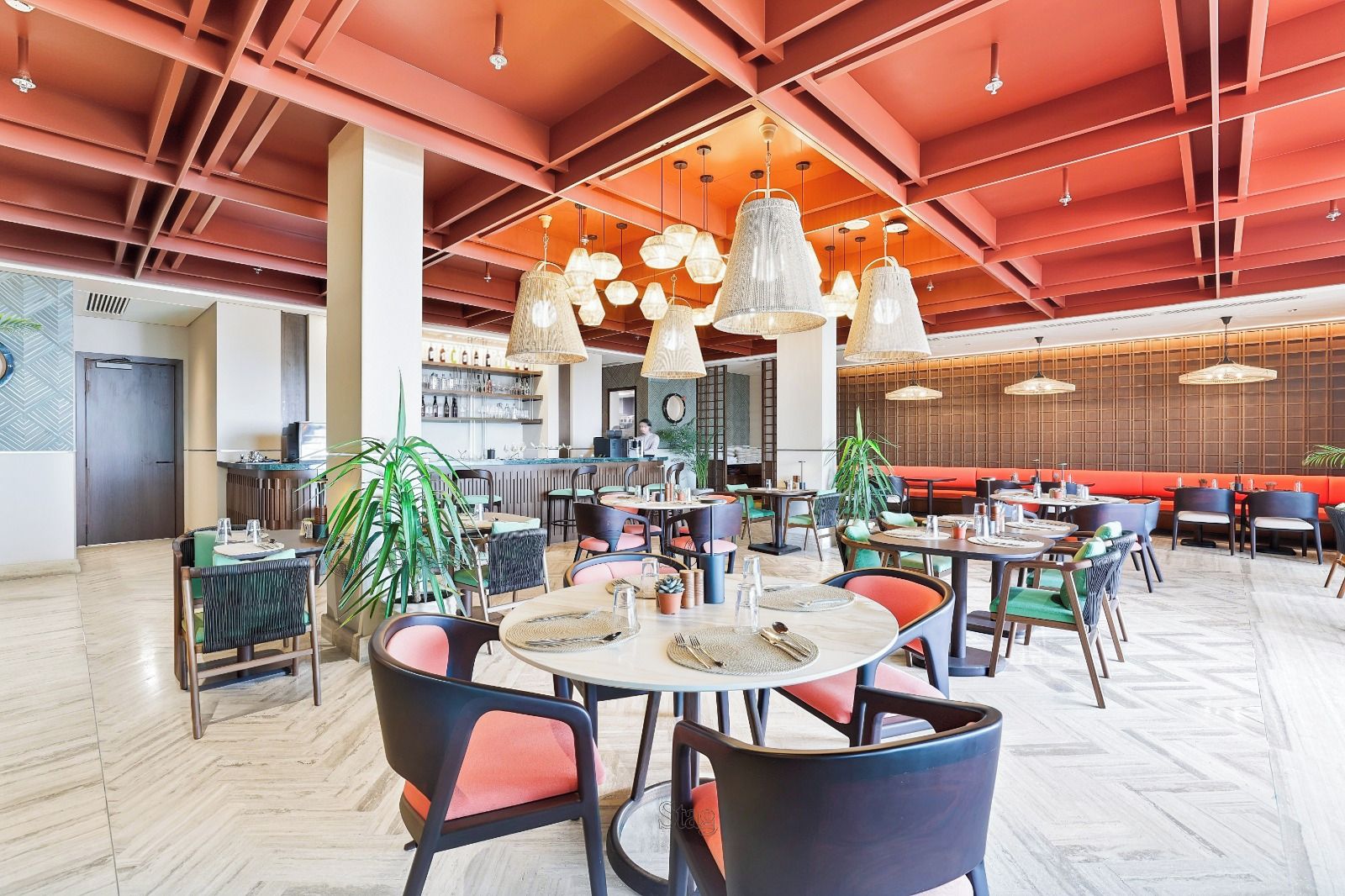 A spacious indoor dining area with round tables and chairs, a bar in the background, and a high ceiling with exposed beams.