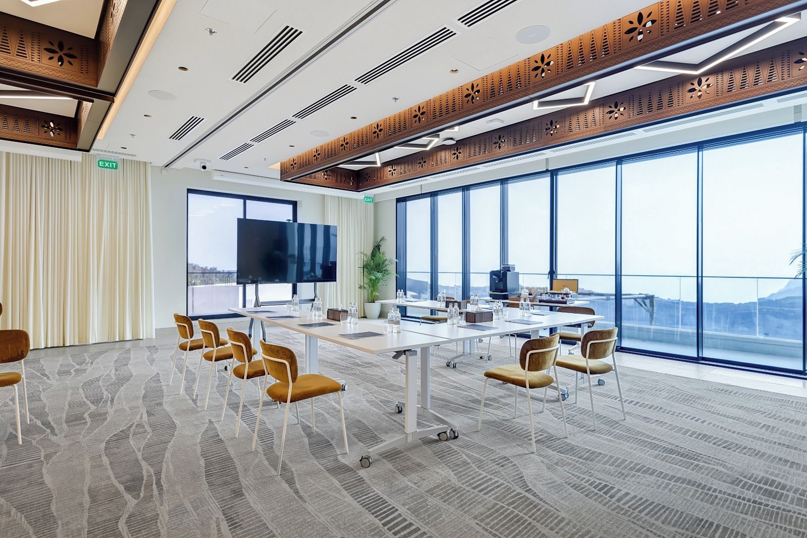 Un salón de conferencias con una mesa grande, sillas, un televisor y amplias ventanas con vistas.
