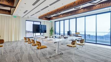 Un salón de conferencias con una mesa grande, sillas, un televisor y amplias ventanas con vistas.
