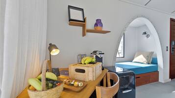 Una habitación moderna con una mesa de madera, una cesta de fruta, una cafetera y una cama con colchón azul.