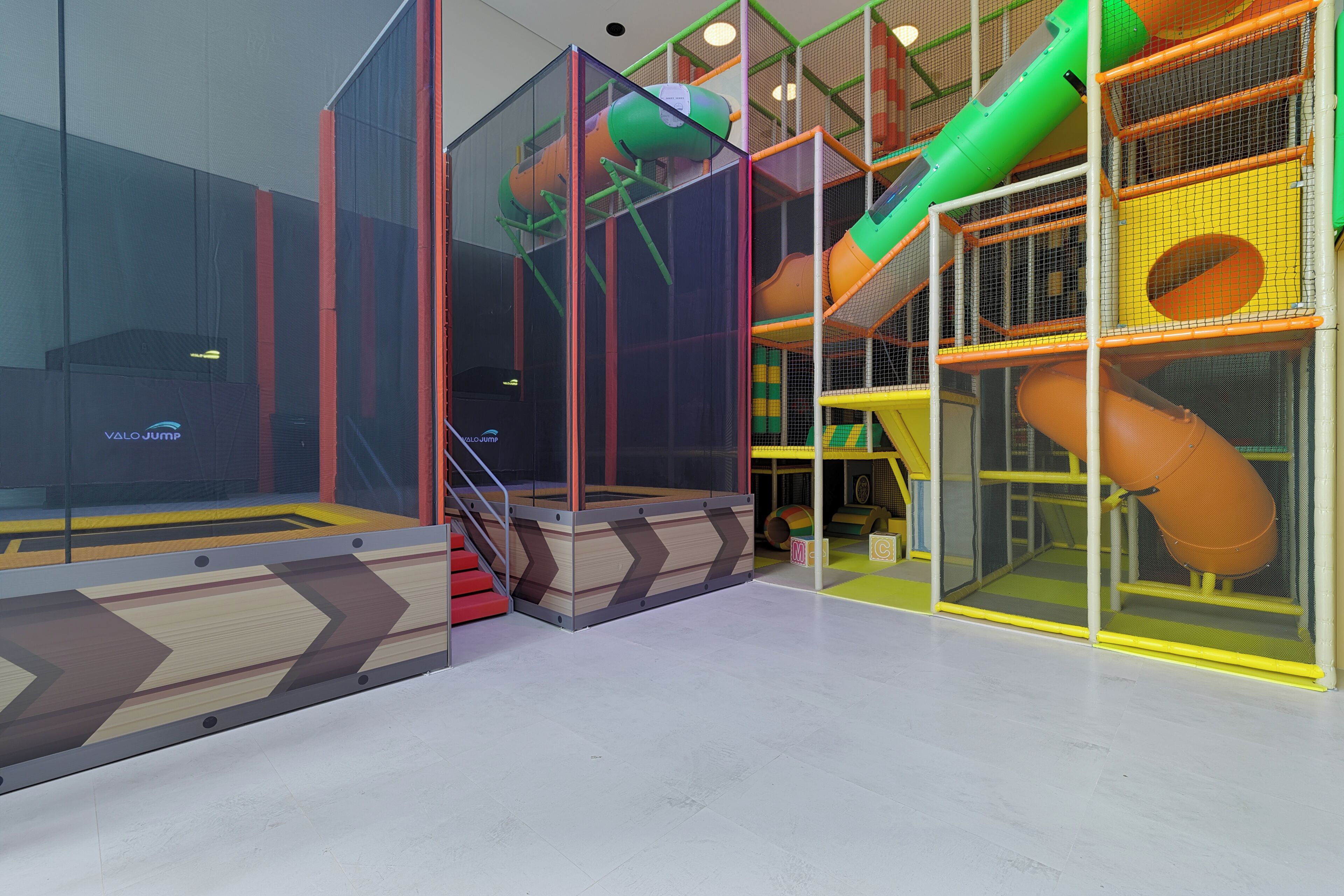 A children's play area with a slide, climbing net, and soft play surfaces.