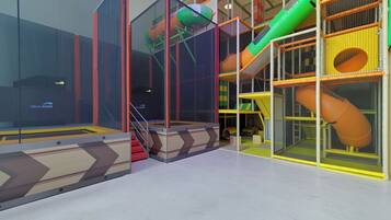 A children's play area with a slide, climbing net, and soft play surfaces.