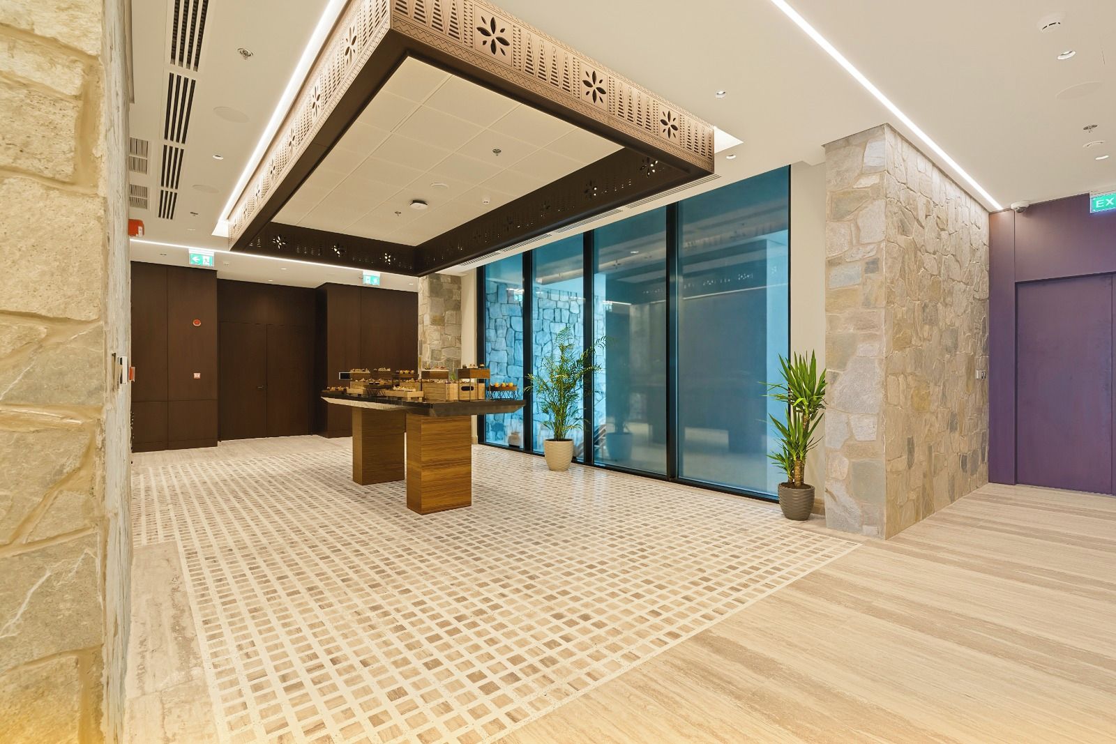 A lobby with a reception desk, stone walls, a patterned floor, and a glass door leading outside.