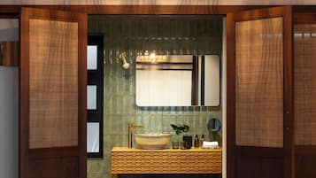 Un dormitorio con cama, un banco, un baño con espejo y una lámpara colgante.