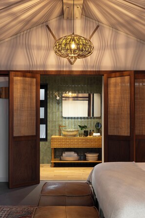 A bedroom with a bed, a bench, a bathroom with a mirror, and a hanging light fixture.