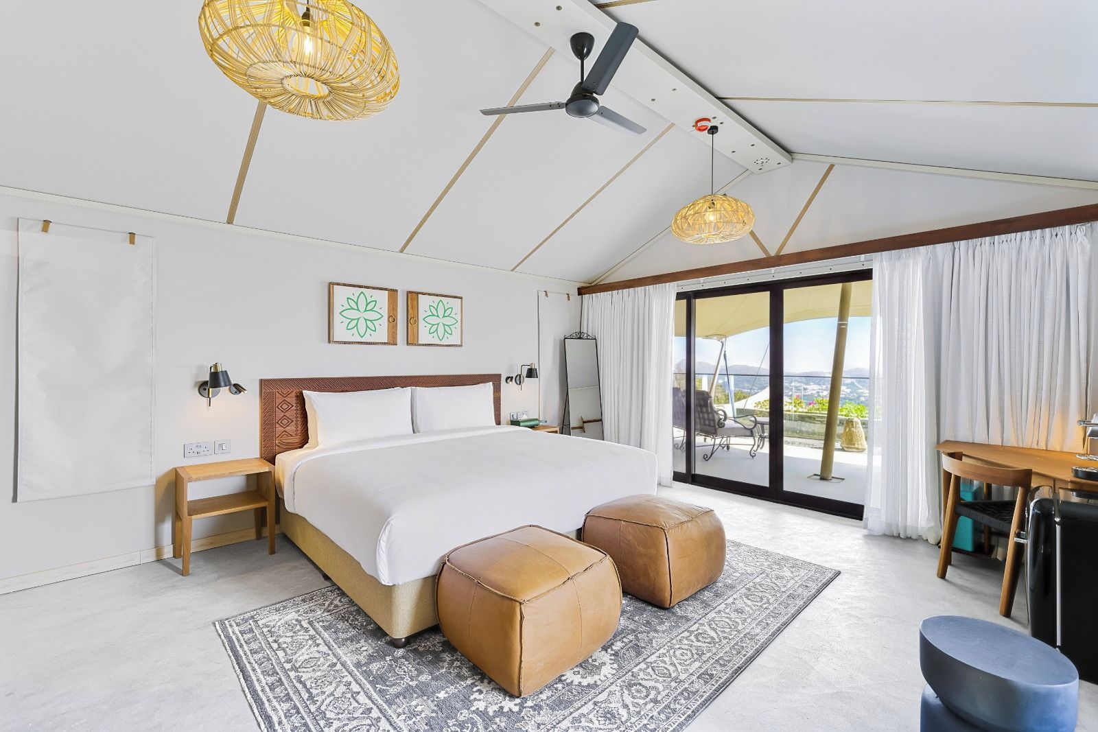 Quarto de hotel moderno com uma cama grande, dois banquinhos, uma escrivaninha e varanda com vista.