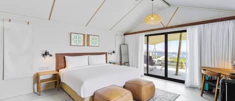 Habitación de hotel moderna con una cama grande, dos reposapiés, un escritorio y un balcón con vistas.