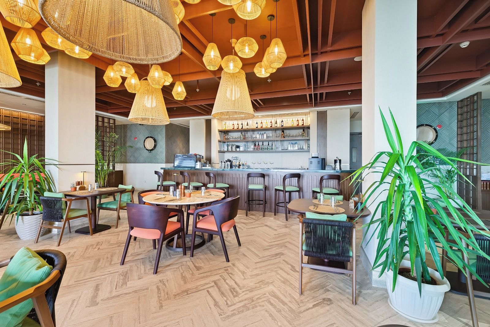 Un vestíbulo de hotel con zona de bar, mesas redondas, sillas y plantas en macetas.