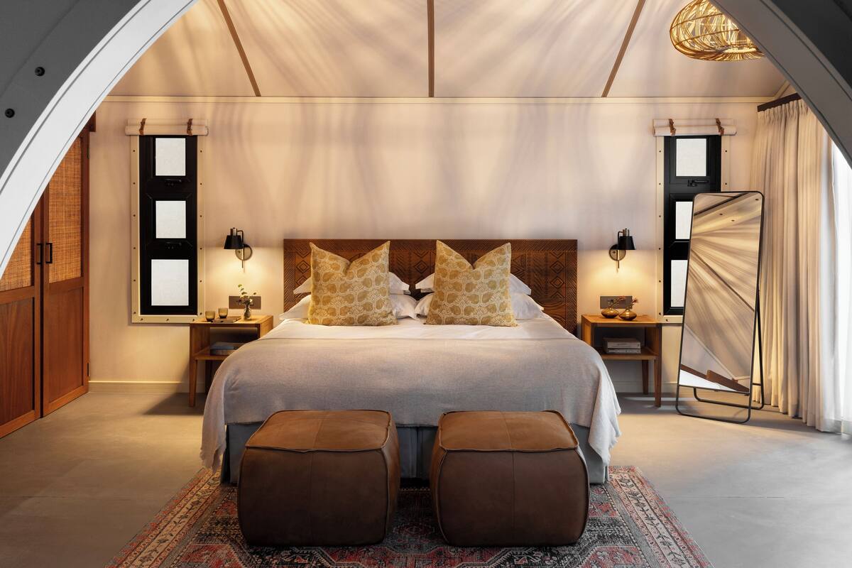 A bedroom with a large bed, two bedside tables, a hanging light fixture, and a view of the outdoors.