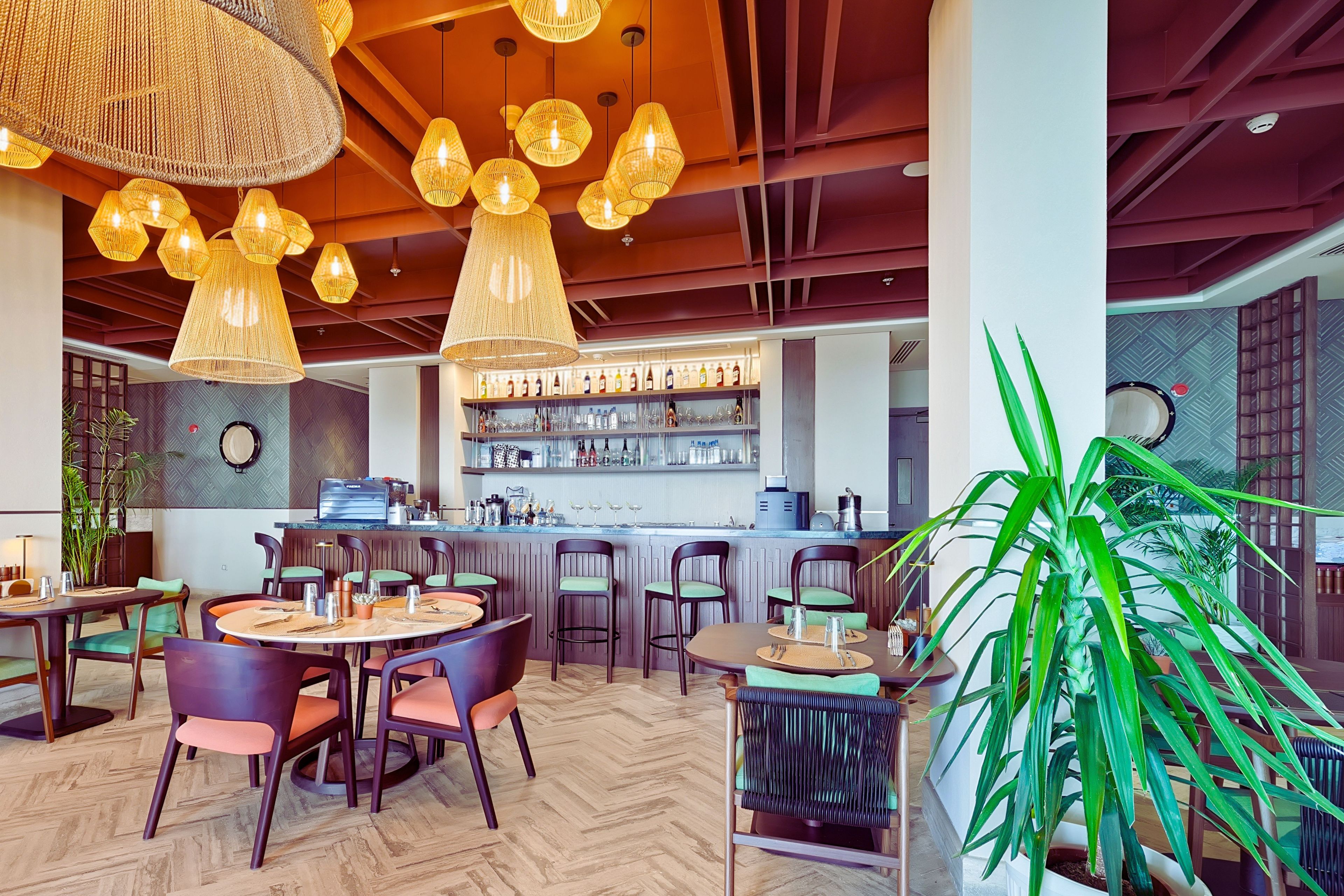 Interior de restaurant amb taules rodones, seients de bar i llums penjants.