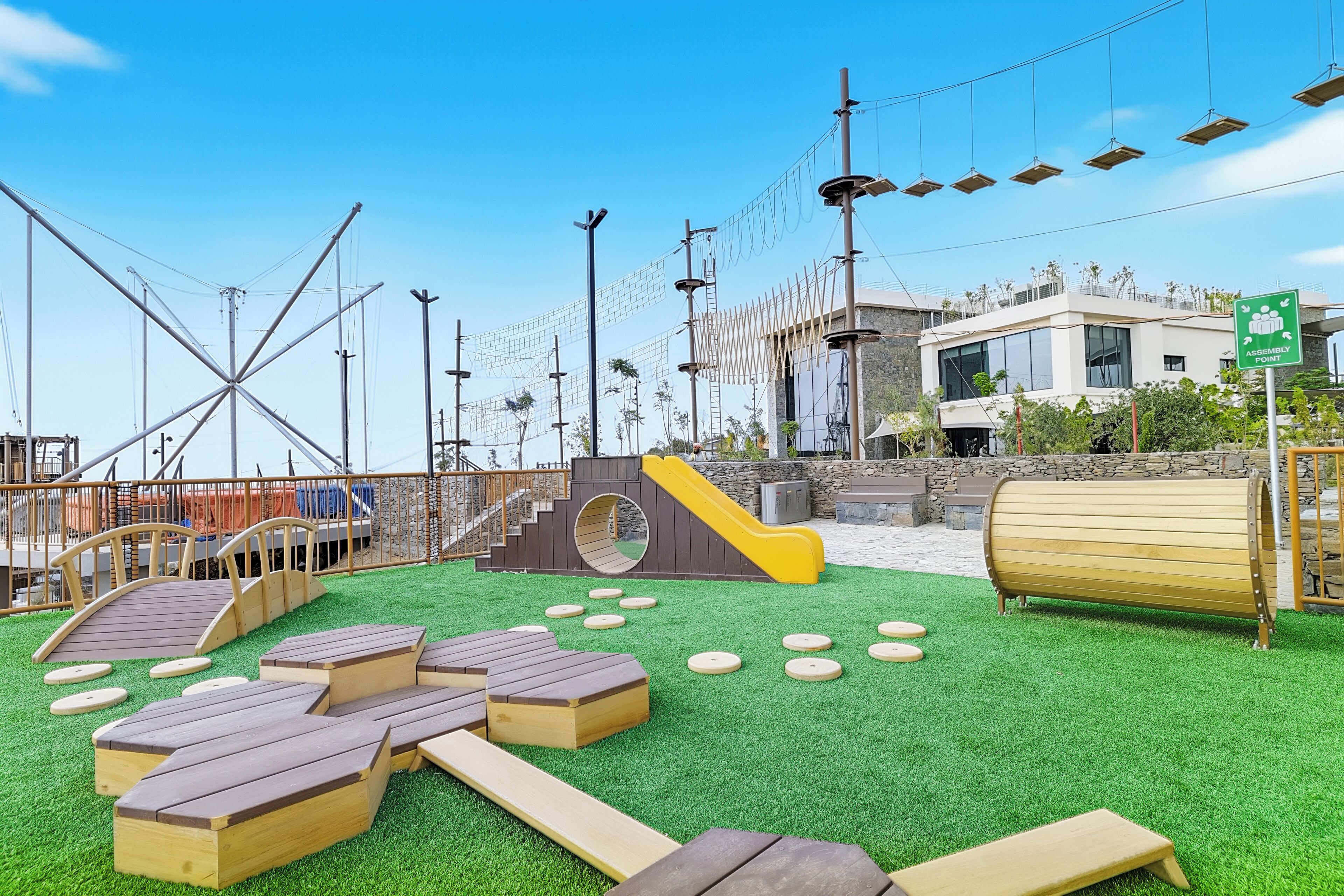 An outdoor play area with artificial grass, wooden play structures, and a slide.