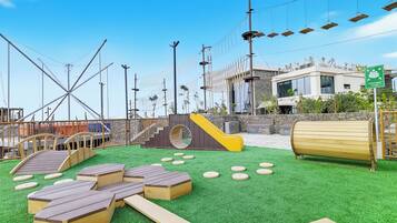 An outdoor play area with artificial grass, wooden play structures, and a slide.