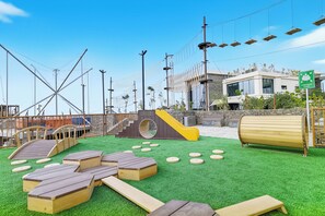 An outdoor play area with artificial grass, wooden play structures, and a slide.