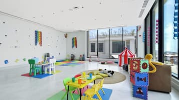 Habitación amplia y luminosa, con un gran ventanal, alfombras de juego coloridas y diversos juguetes y muebles para niños.