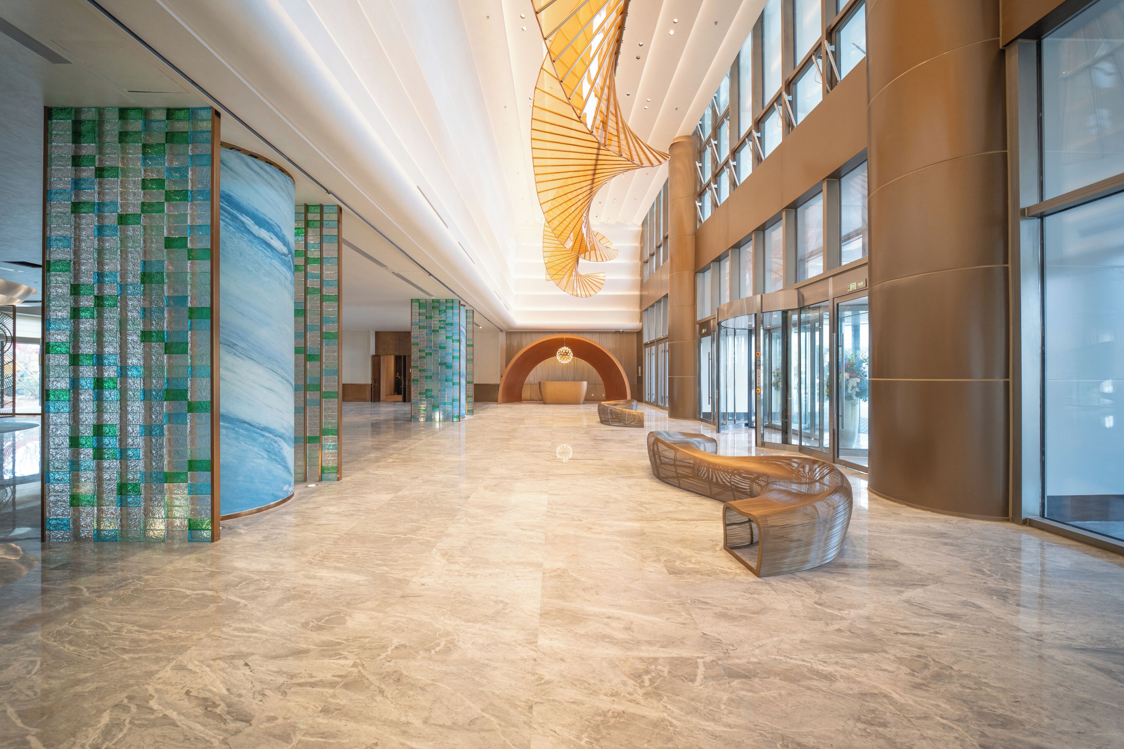 A spacious lobby with a marble floor, a large curved bench, and a distinctive ceiling design.