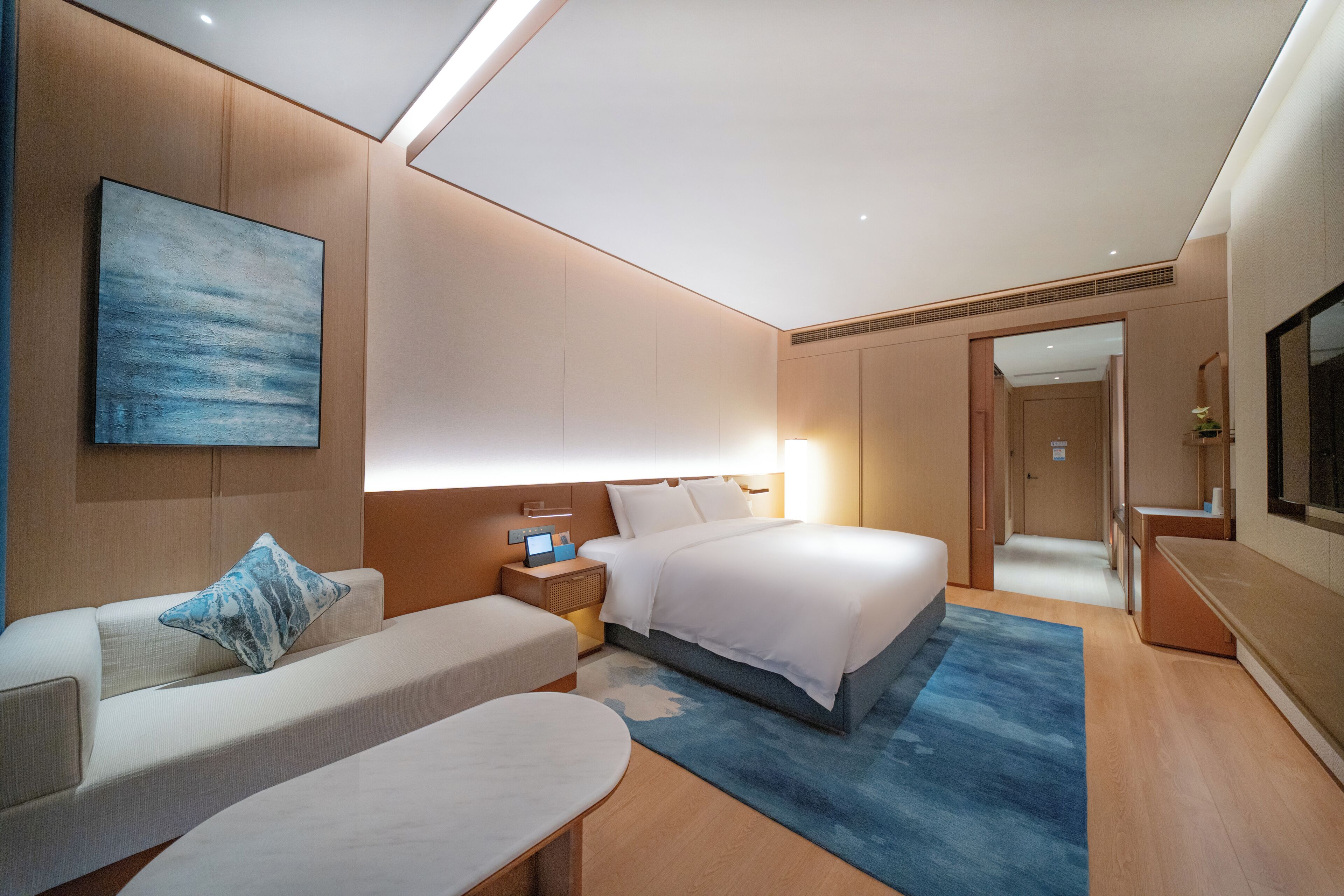 Una habitación de hotel moderna con una cama, un sofá, una mesita de noche, una lámpara y un cuadro en la pared.