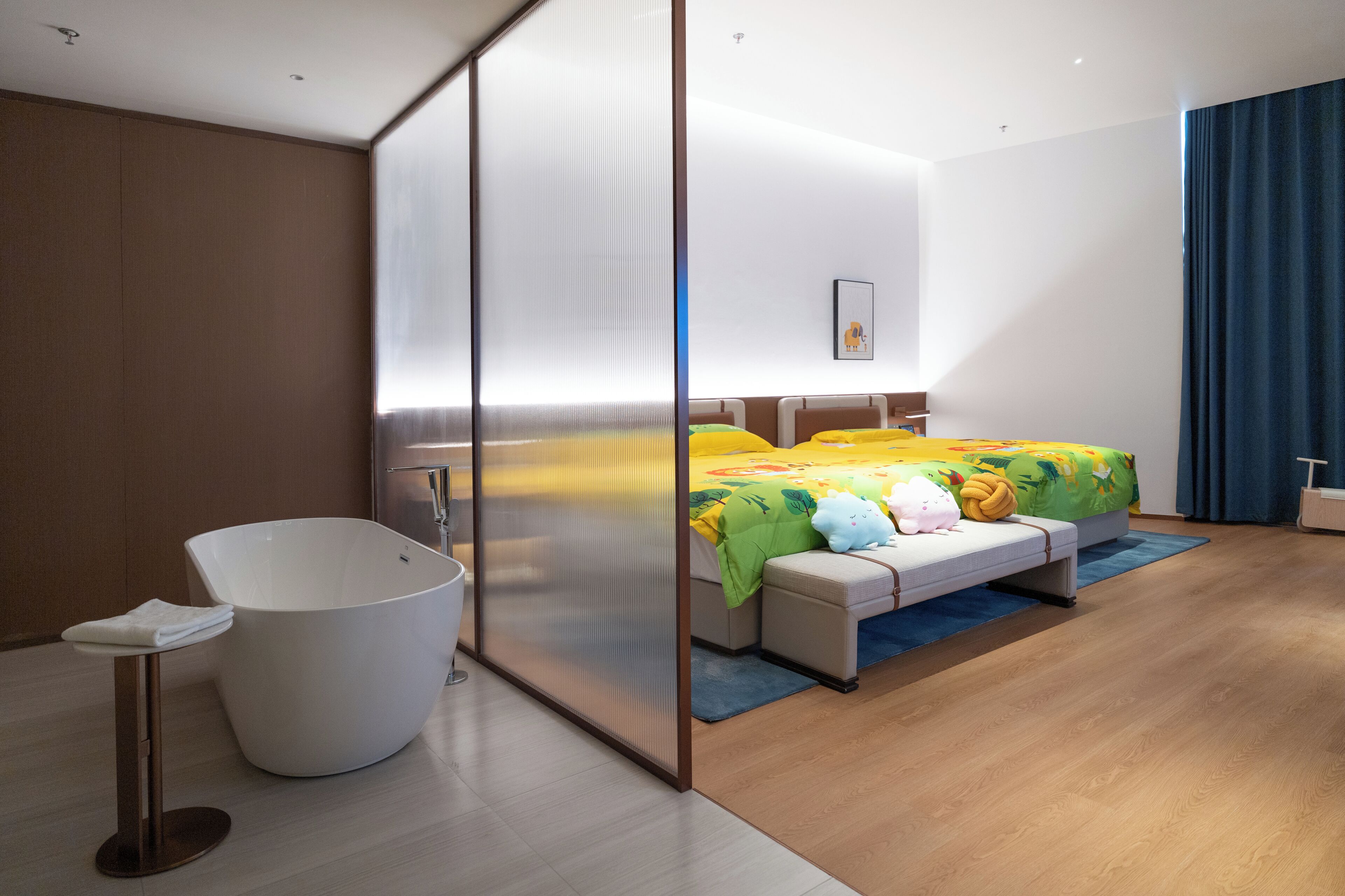 Une chambre d’hôtel moderne dotée d’une grande baignoire, d’un lit avec une literie aux couleurs vives, d’un petit coin salon et d’une grande fenêtre avec des rideaux.