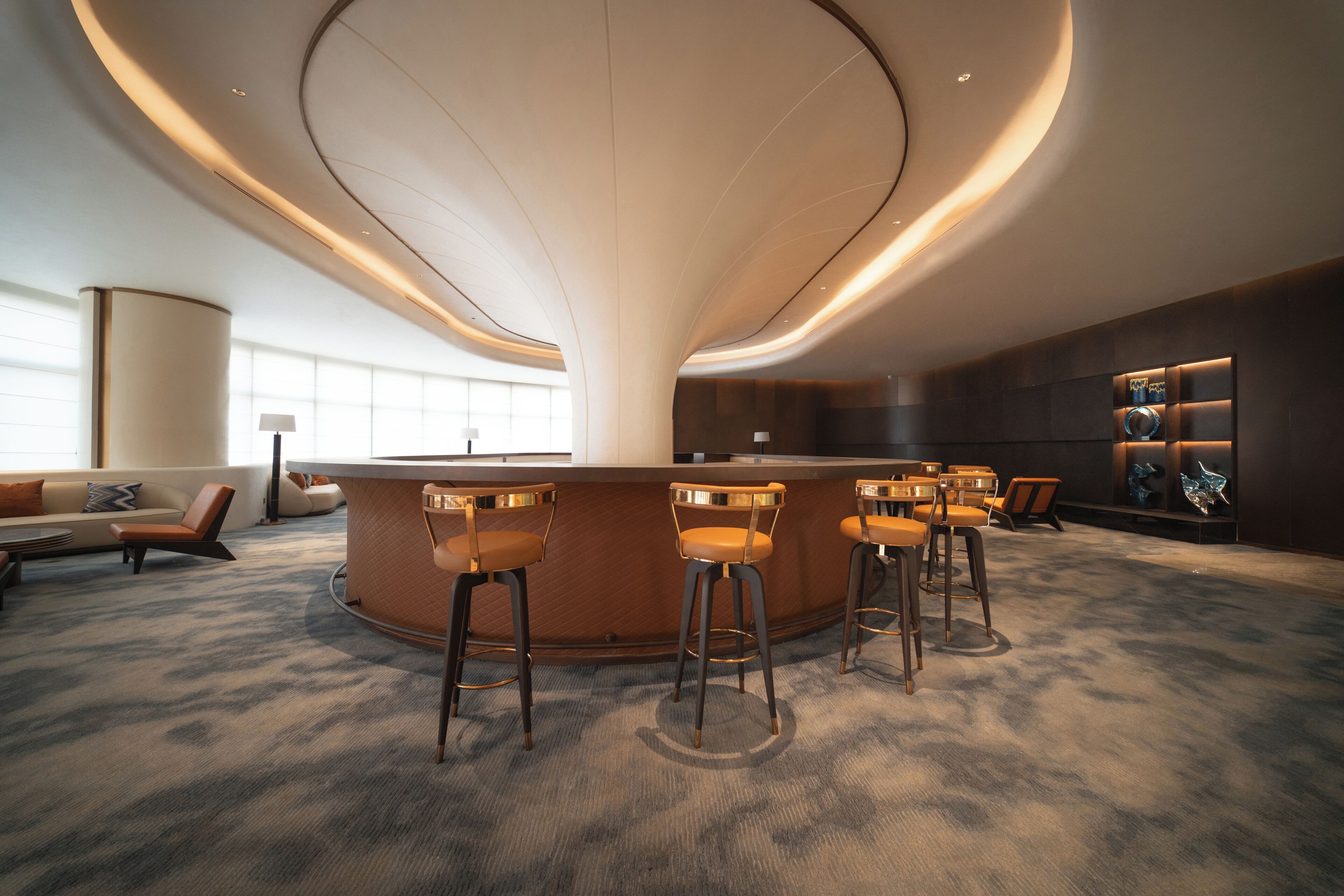 A modern bar area with a curved ceiling, bar stools, and a seating area with a sofa and chairs.