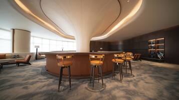 A modern bar area with a curved ceiling, bar stools, and a seating area with a sofa and chairs.