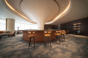 A modern bar area with a curved ceiling, bar stools, and a seating area with a sofa and chairs.
