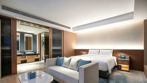 Una habitación de hotel moderna con cama, sofá, mesita de noche y baño visible a través de una puerta abierta.