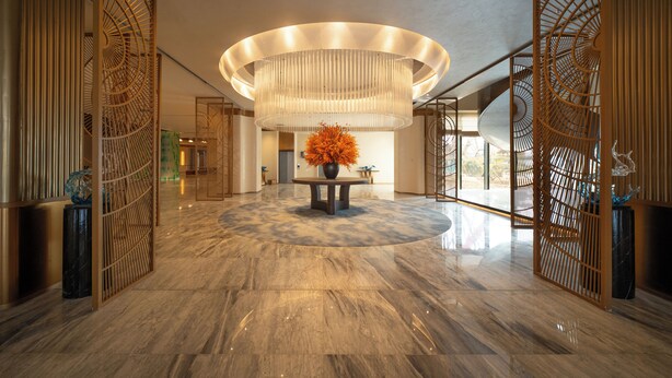Un vestíbulo con piso de mármol, una mesa central con un florero y una lámpara circular grande.
