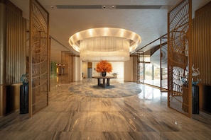 A lobby with a marble floor, a central table with a vase, and a large circular light fixture.